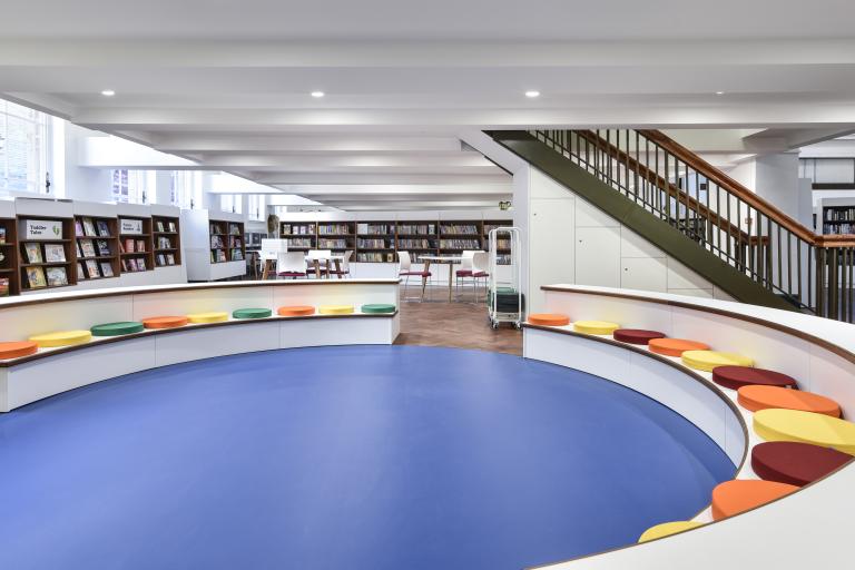 A social space inside Bolton Central Library. A blue soft floor is surrounded by an oval seating area.