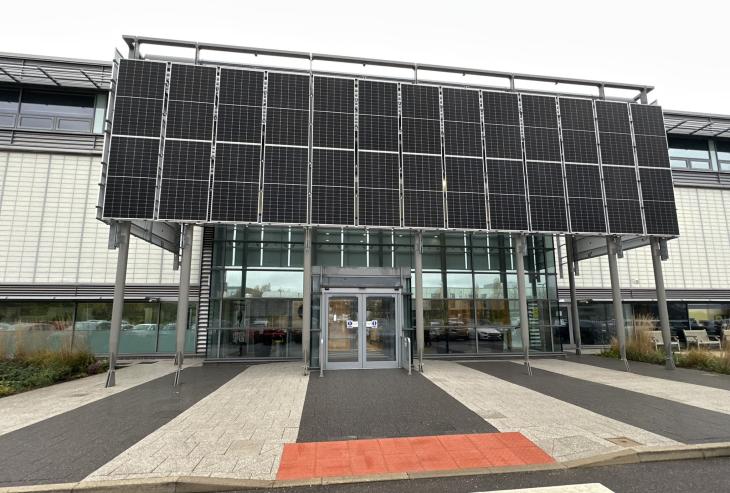 The front of the Factory of the Future, at the AMRC net zero refurbishment. The image shows the front door with glass panels around it and two large rows of solar panels above.