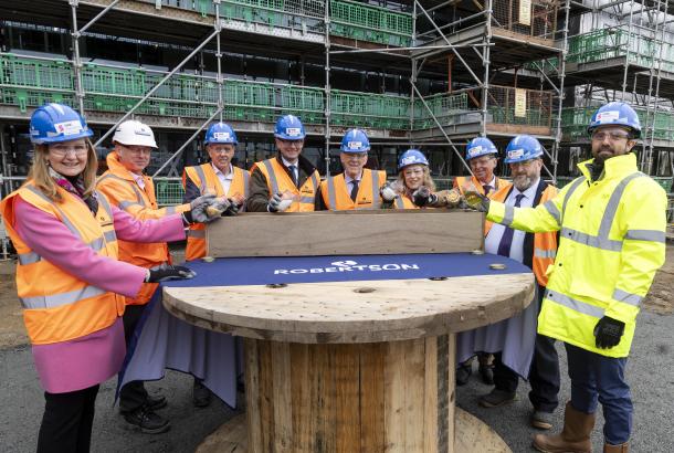 People surrounding a table at a construction site pouring ingredients into a brick mould