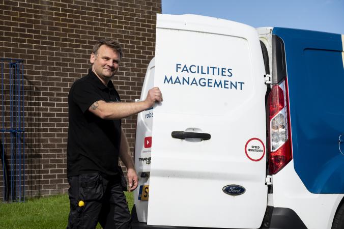 A Robertson Facilities Management engineer holding the back door of an electric vehicle open. 