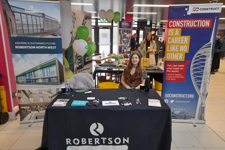 Robertson Construction Social Impact Manager sat behind a table with banners at a college's careers event