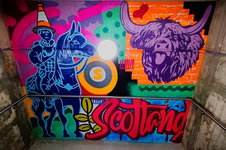 Graffiti paint in the wall of a student accommodation's stairwell, depicting Scotland with a Highland Coo, Duke of Wellington and bold colours 