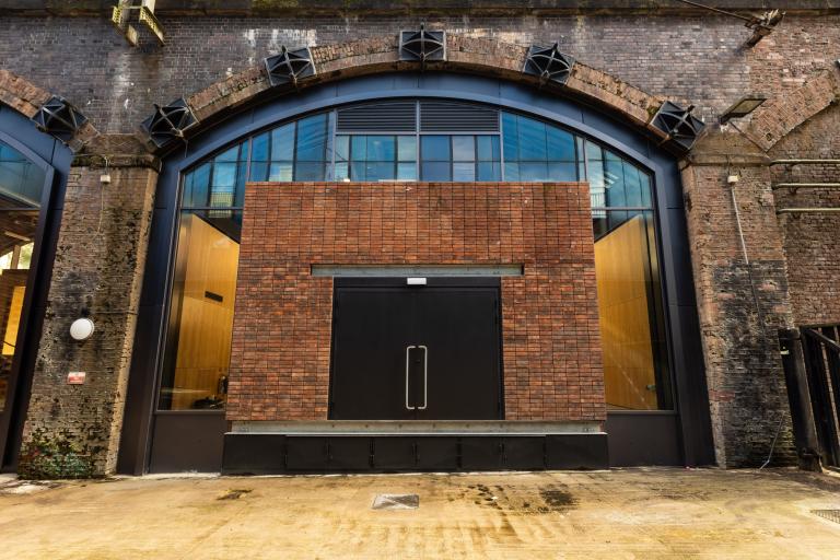 Main entrance of the new HOME Arches in Manchester, showing a red-brick facade within an existing railway arch and black double doors