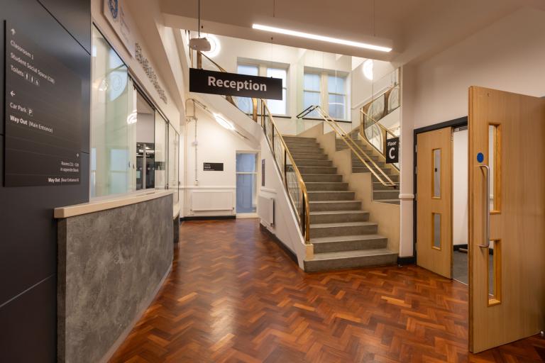 Reception area of a university building, featuring herringbone floor, historic staircase and newly refurbished areas