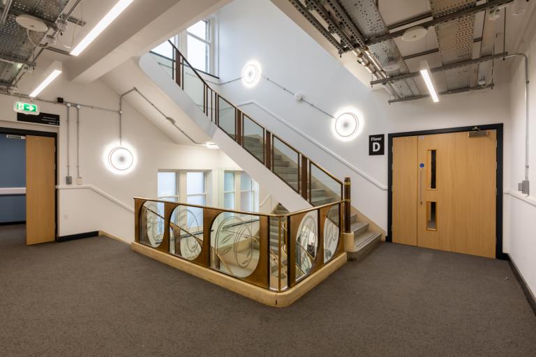 Landing of a university building's staircase, showing a well-lit area with glass panelling and new furnishings