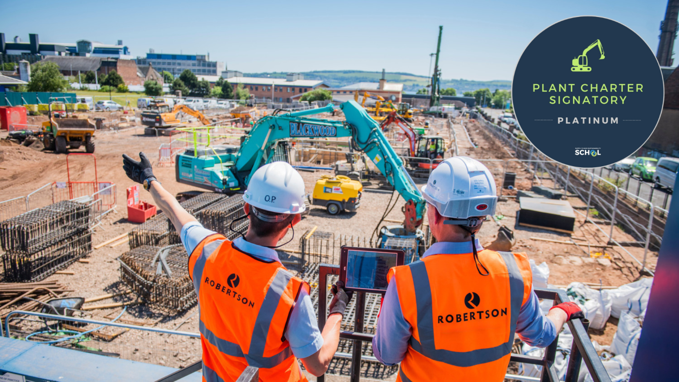 People in personal protective equipment looking out to a construction site containing plant machinery and stored materials