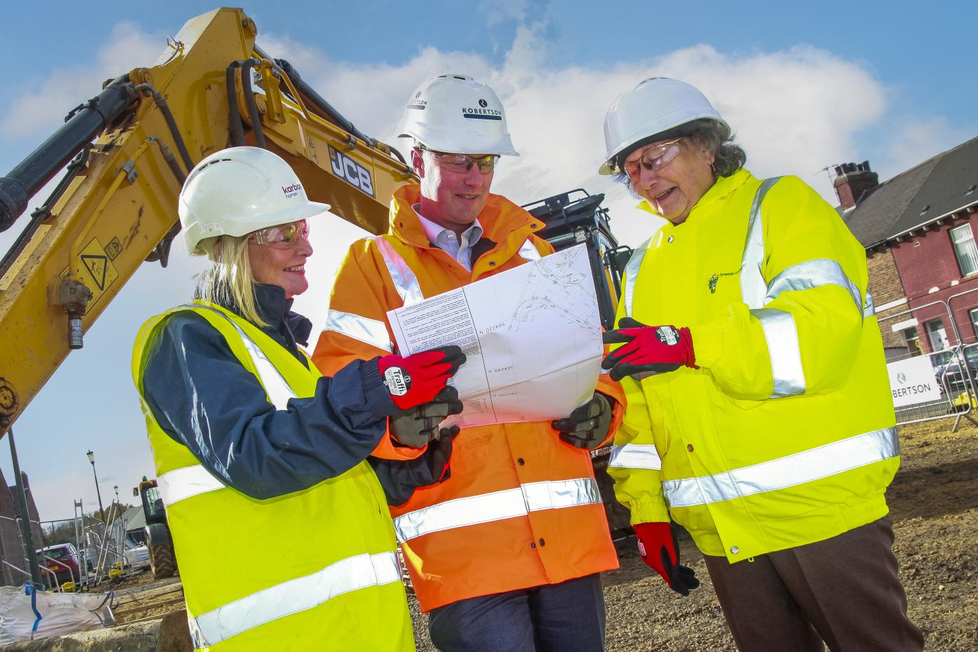 people looking at construction plans in PPE in front of an excavator