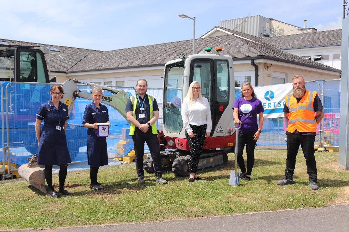 Six people standing in front of mini digger